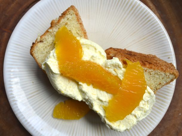Overhead view of a slice of mimosa cake, served on a white plate and topped with orange cream and scattered with orange segments.