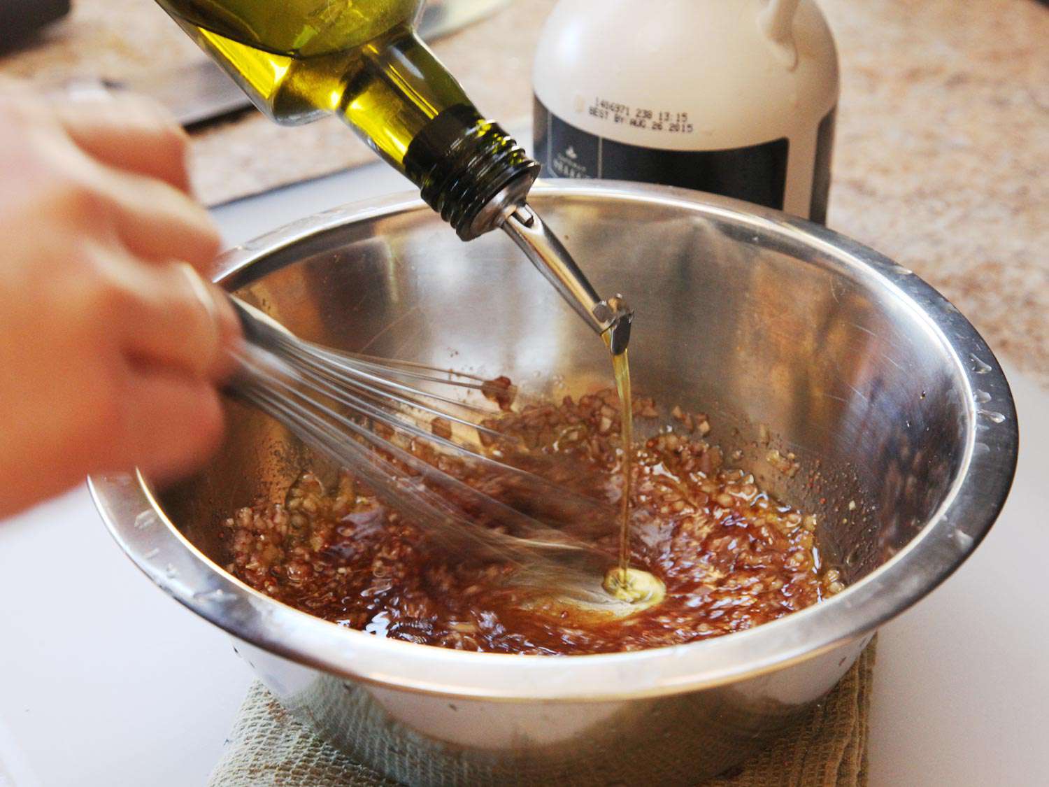 Drizzling olive oil in a mixing bowl containing vinaigrette for the salad. 
