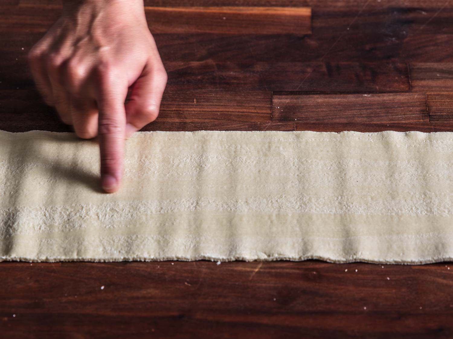 Finger pointing out horizontal striping on ramen dough sheet