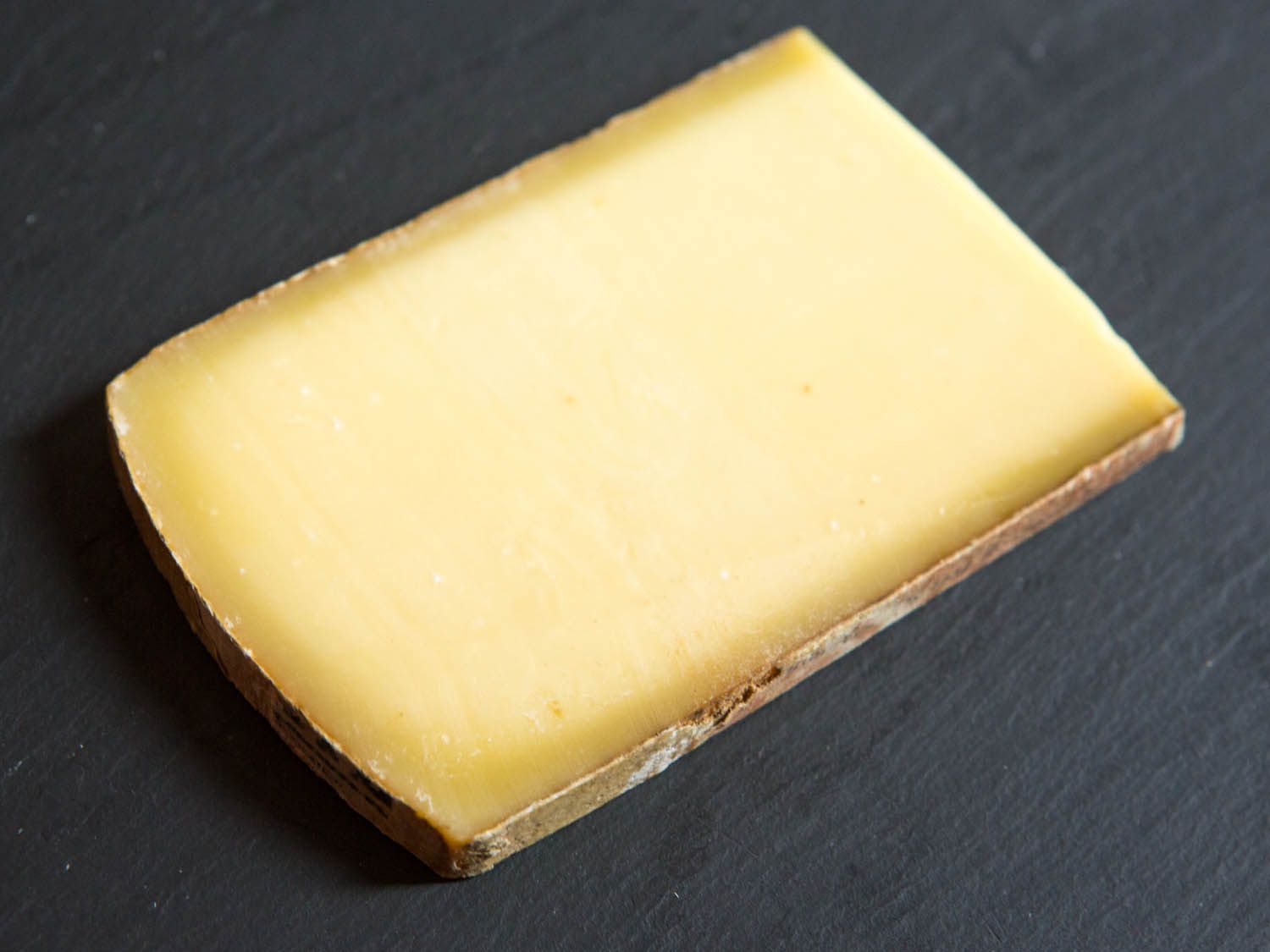 A narrow slice of Comté on a black board.