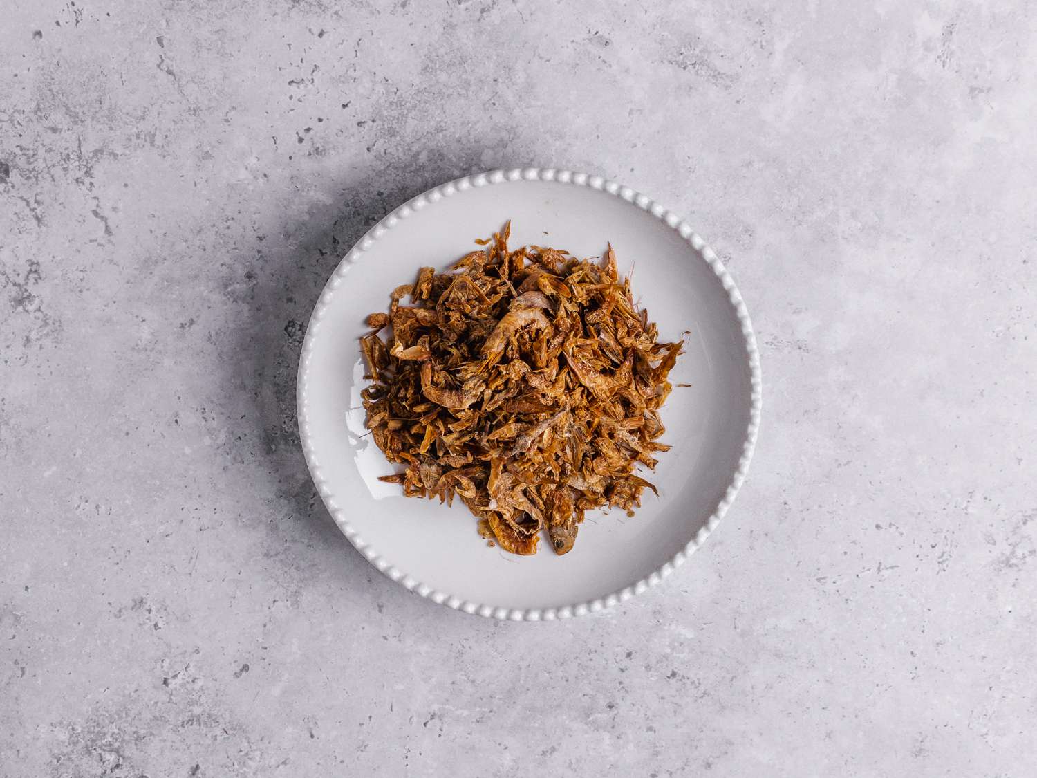 Dried crayfish in a white bowl on a marbled grey background