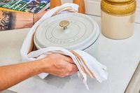 A person picking up and holding onto a Dutch oven with a kitchen towel.