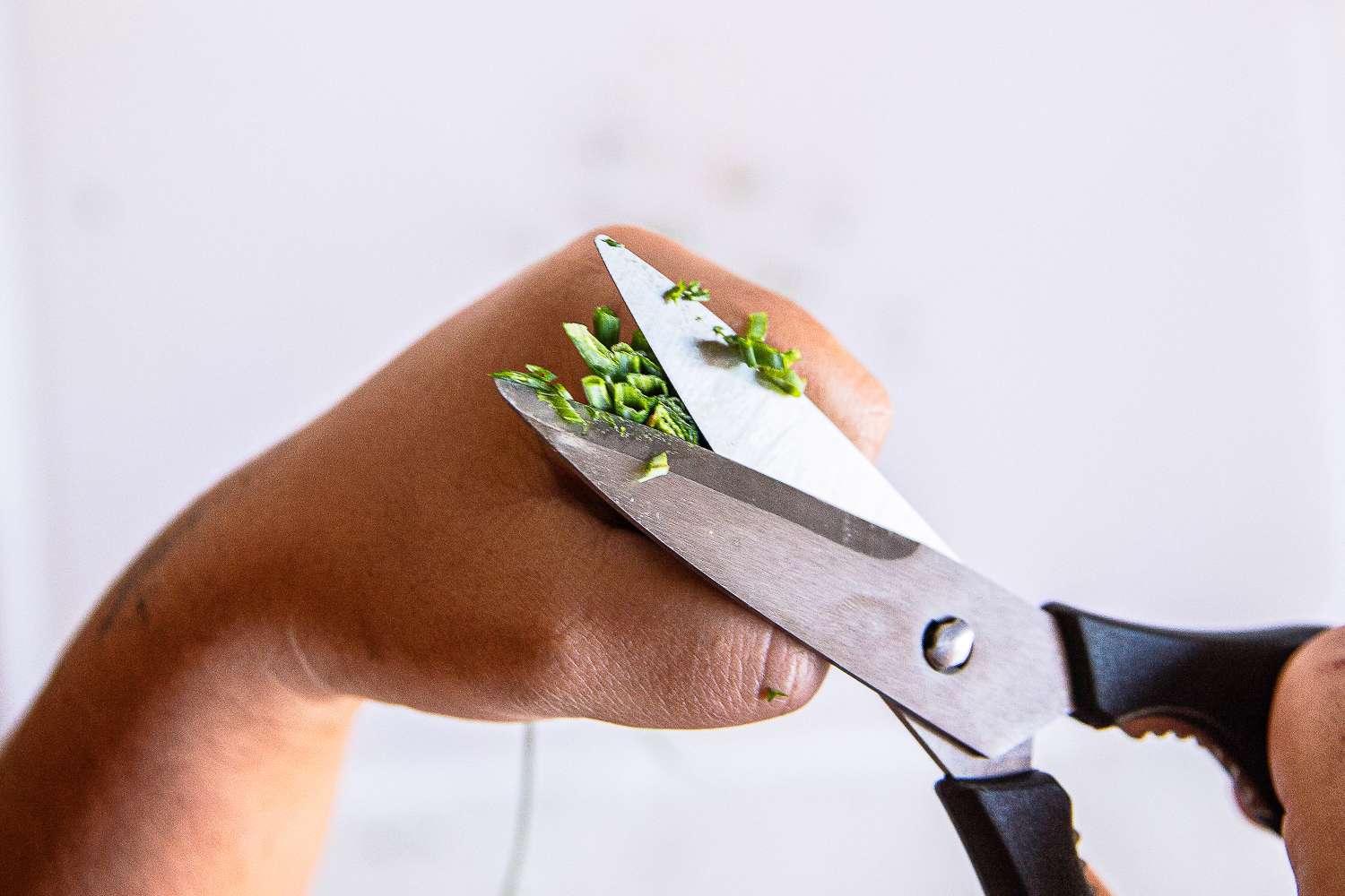 A hand using Wüsthof scissors to cut small pieces of green herbs