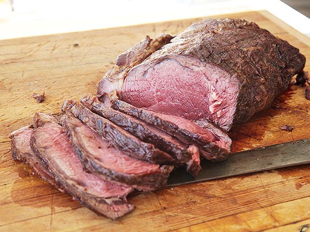 A grilled bison rib roast, carved on a cutting board, slices shingled.