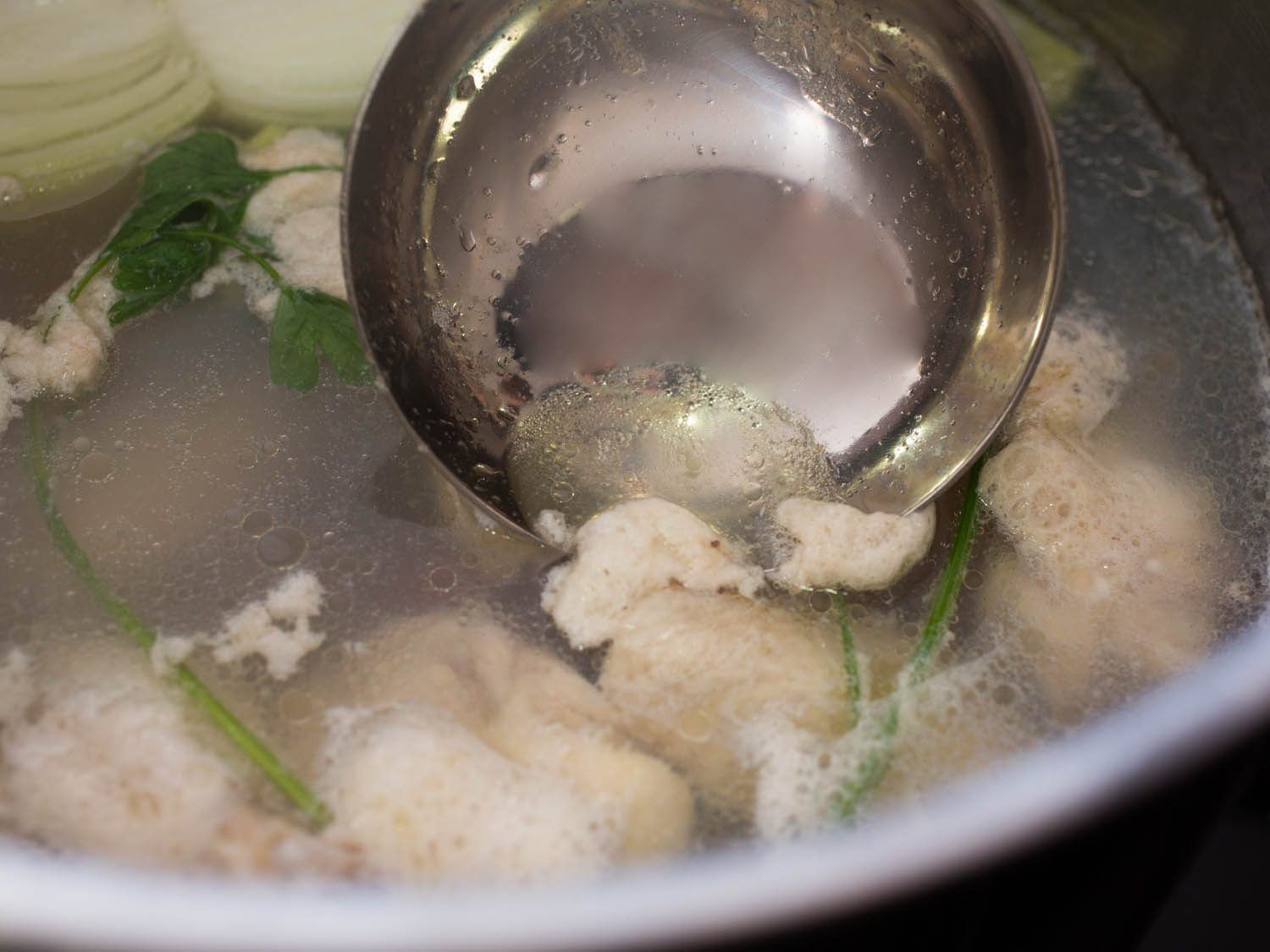Skimming scum from the surface of stock with ladle.