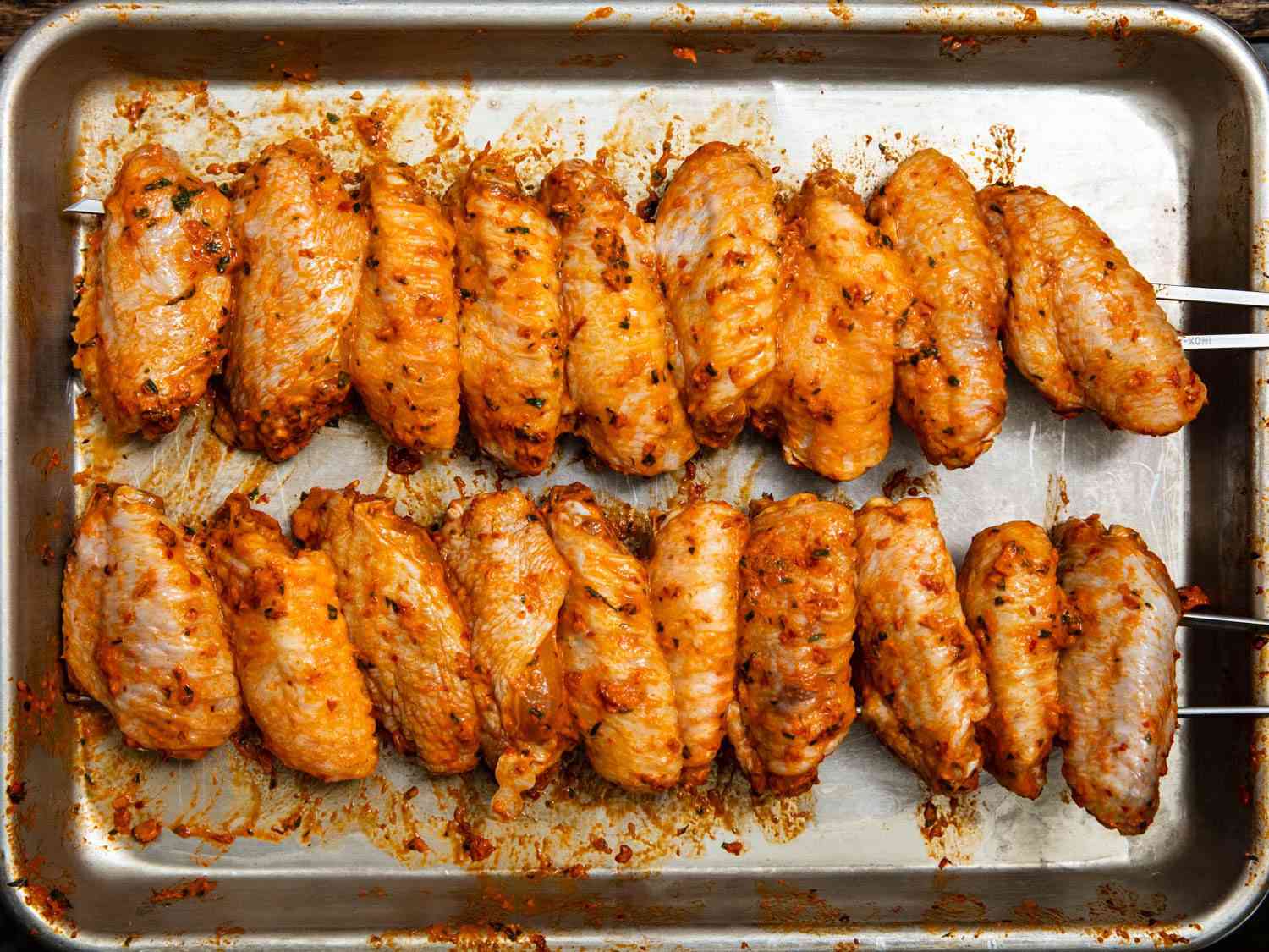 Overhead shot of a tray of skewered Turkish chicken wings rubbed with chile paste, before cooking.