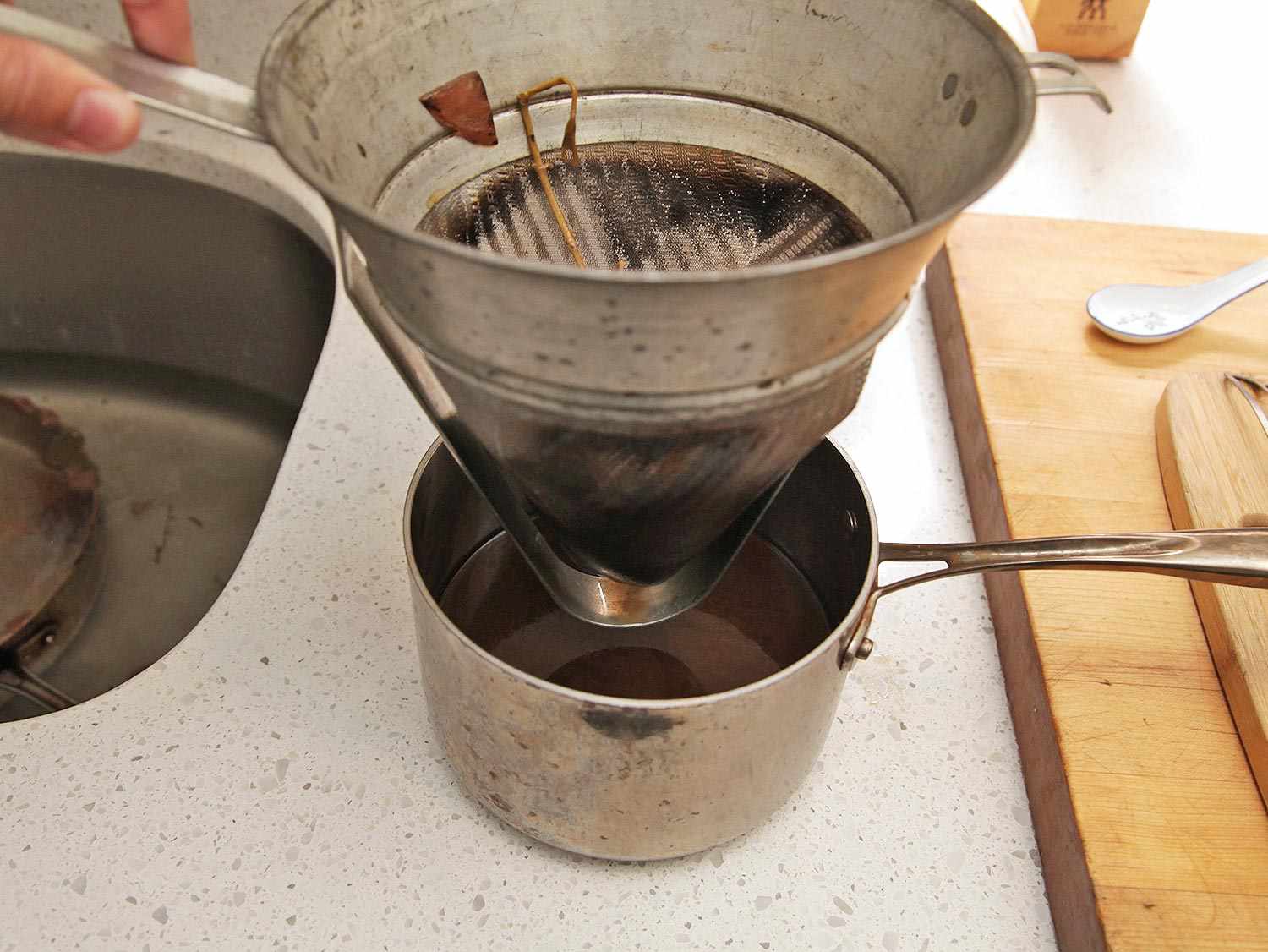 Turkey braising liquid being strained through a fine-mesh strainer into a saucepan. 