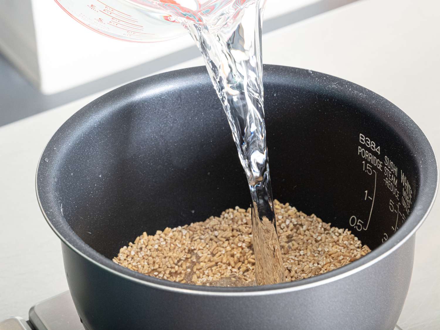 Pouring water into rice cooker with oats in it.