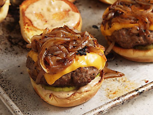 The burgers are topped with melty cheese and fried onions, awaiting their bacon weave layer.