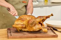A person carving a fully-cooked Grassland Beef Pasture Raised Turkey on a cutting board