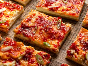 Cheese and pepper jelly tart slices garnished with sesame seeds and green onion pieces on a wooden surface