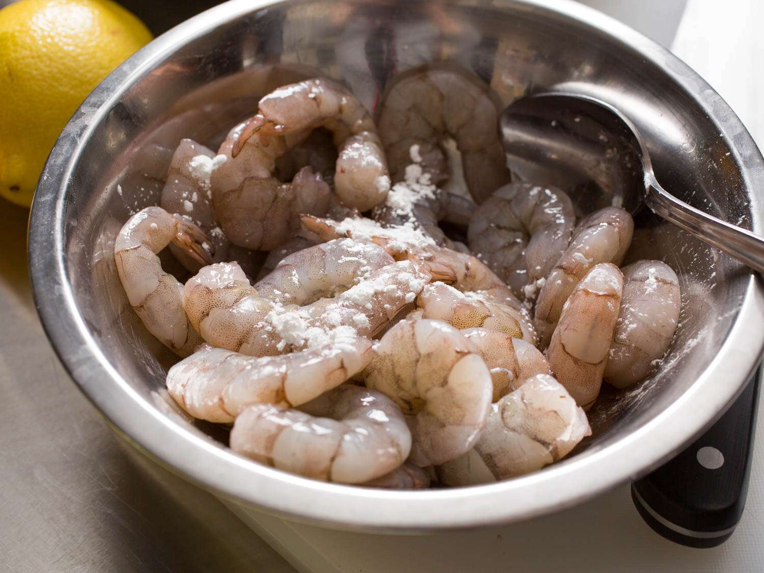 Tossing raw shrimp with baking soda, cornstarch, and salt.