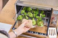 A person removes broccoli from the Breville The Smart Oven Air Fryer Compact