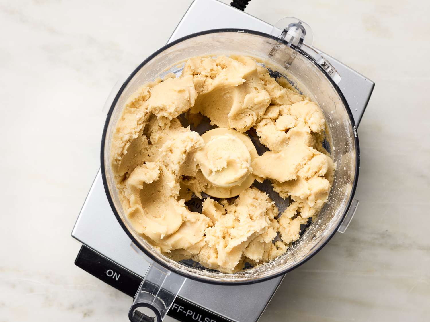 A food processor with dough mixture inside, placed on a countertop