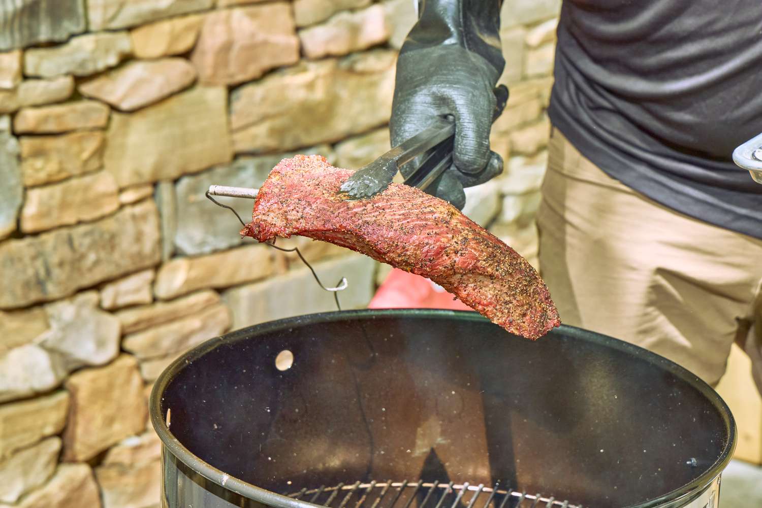 A person cooks meat in the Pit Barrel Cooker Co. Classic Pit Barrel Cooker