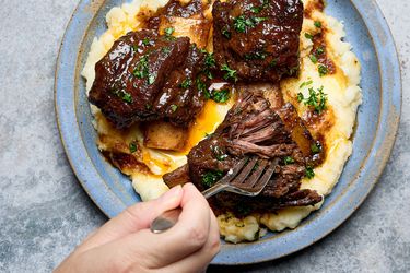 Short ribs served over mashed potatoes with a fork taking a piece