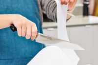 Hands slicing a piece of paper with a Misono UX10 8.2-Inch Gyutou