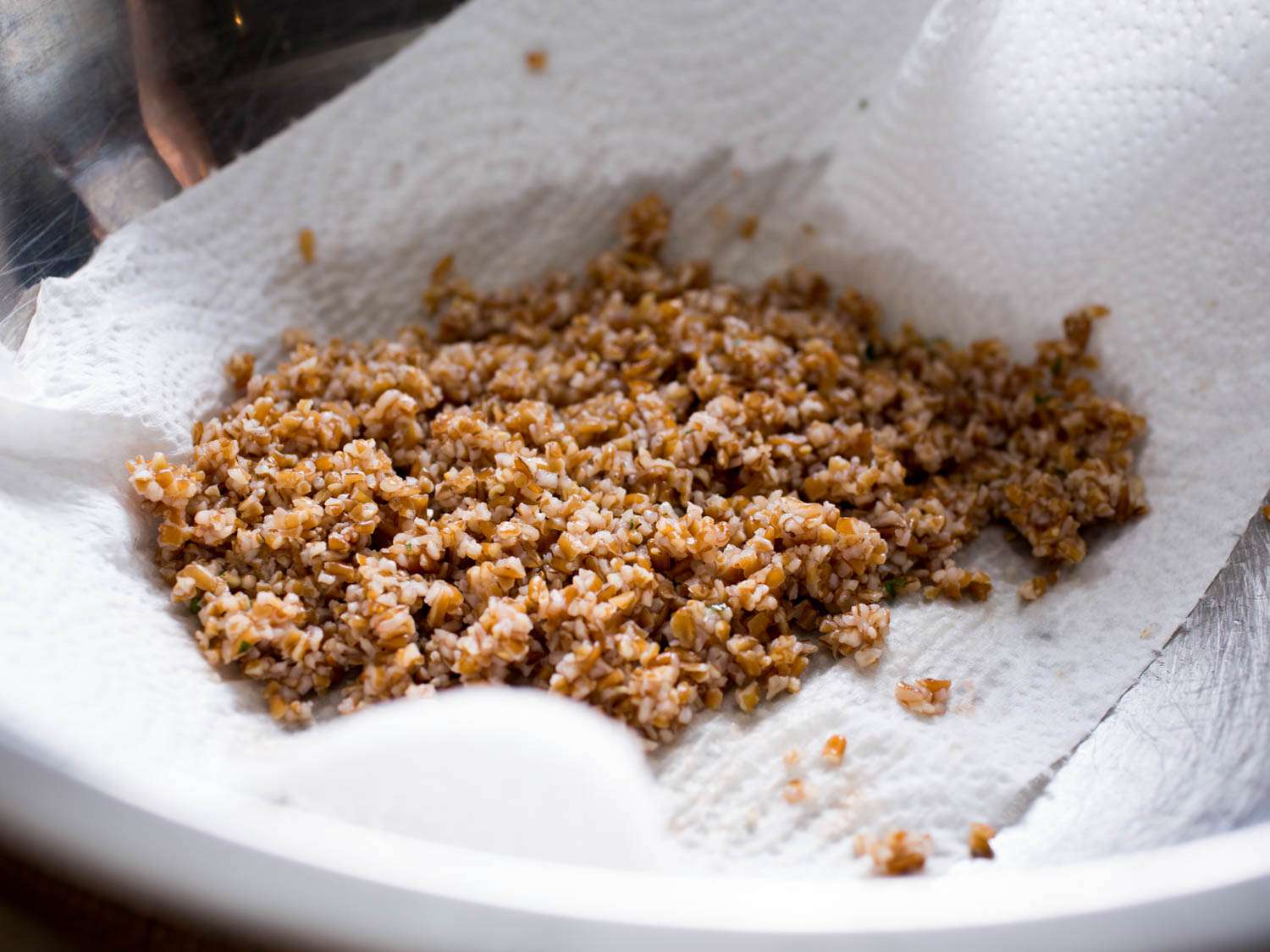 Bulgur draining in a mixing bowl lined with paper towel. 