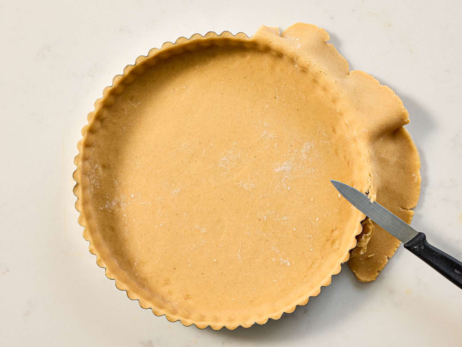 A round pastry being prepared in a tart pan with a knife trimming excess dough