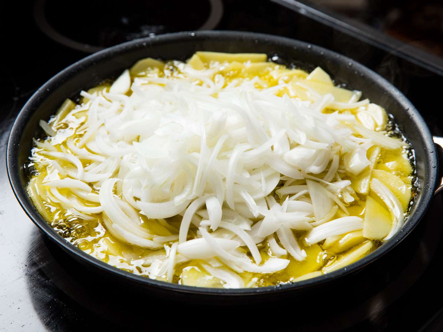 Frying sliced potatoes and onions in a skillet for tortilla española. 