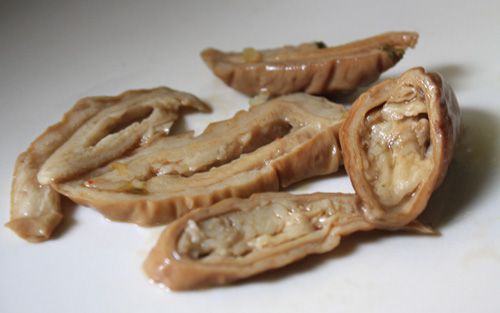 Close-up of sliced, stewed intestine on a white plate.