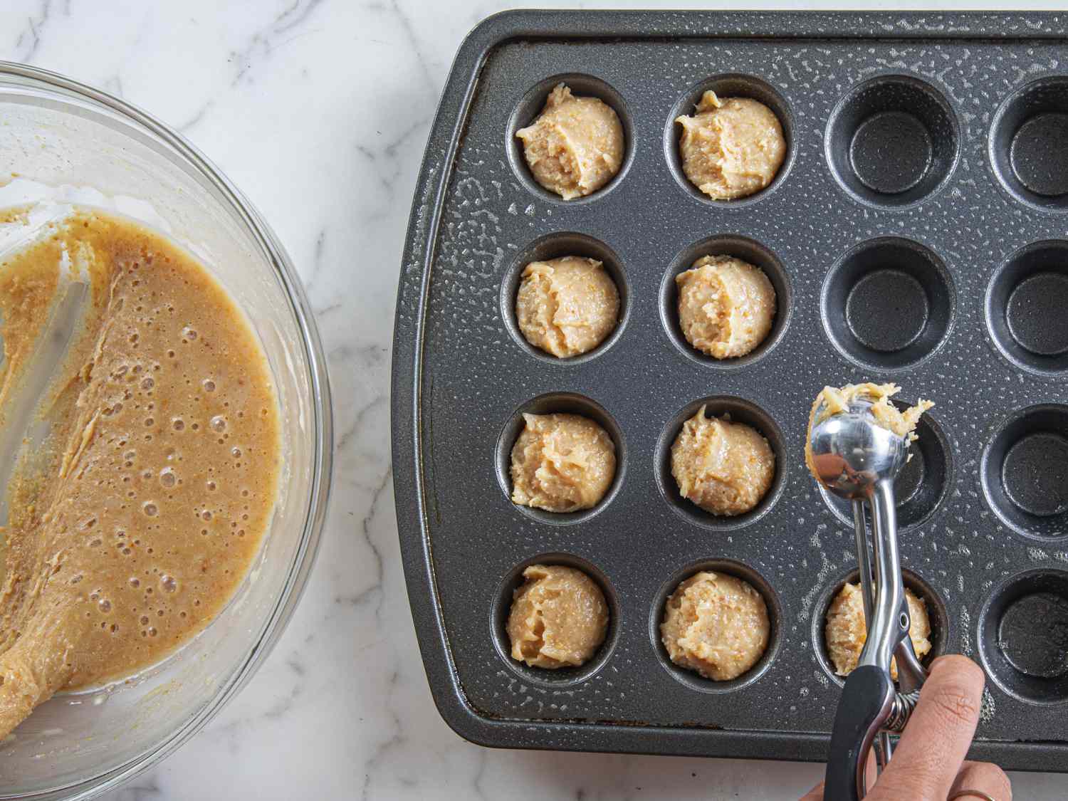 Overhead view of batter being added to a mini cupcake pan
