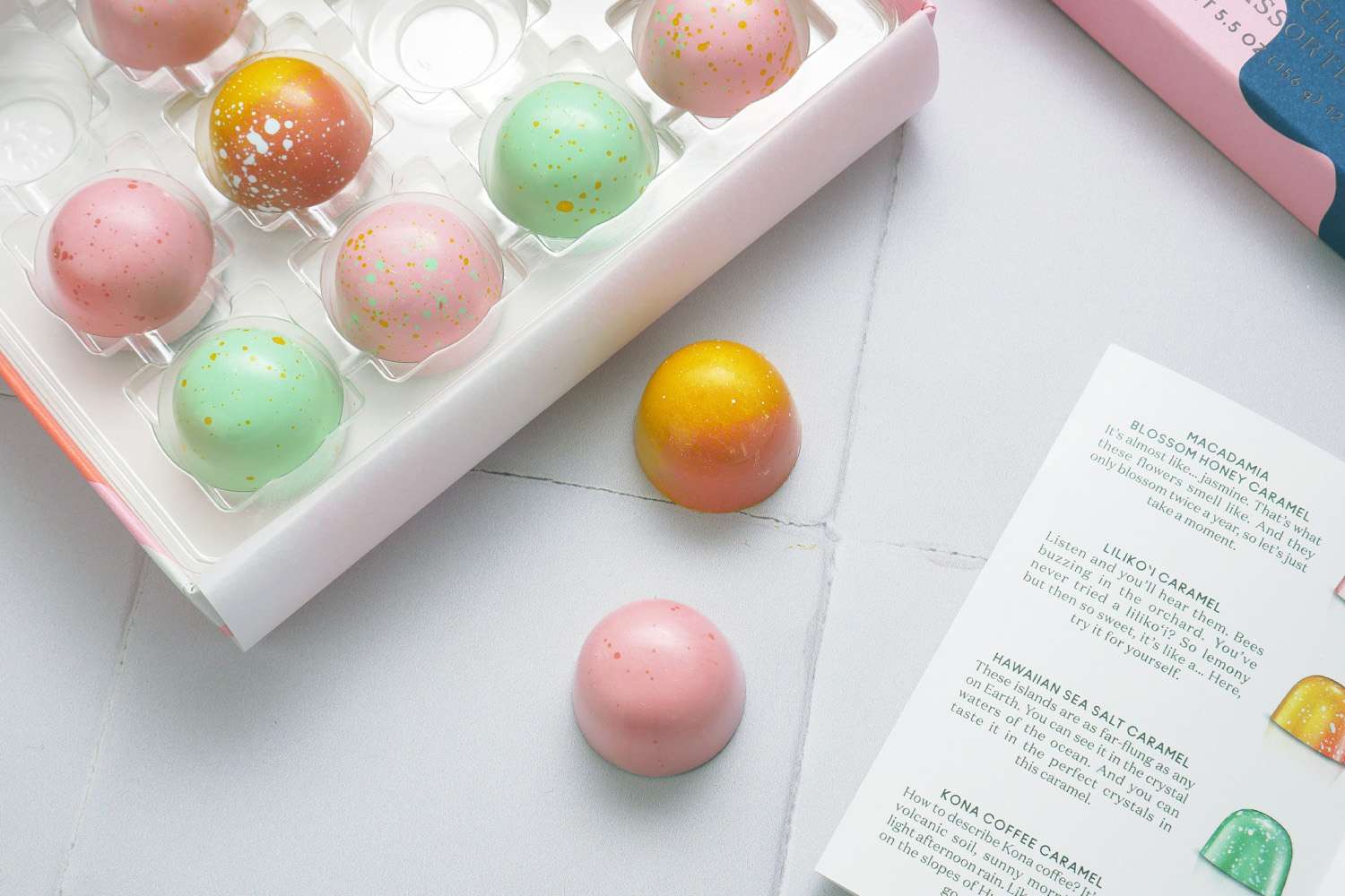 A box of colorful spherical chocolates with a product description card nearby