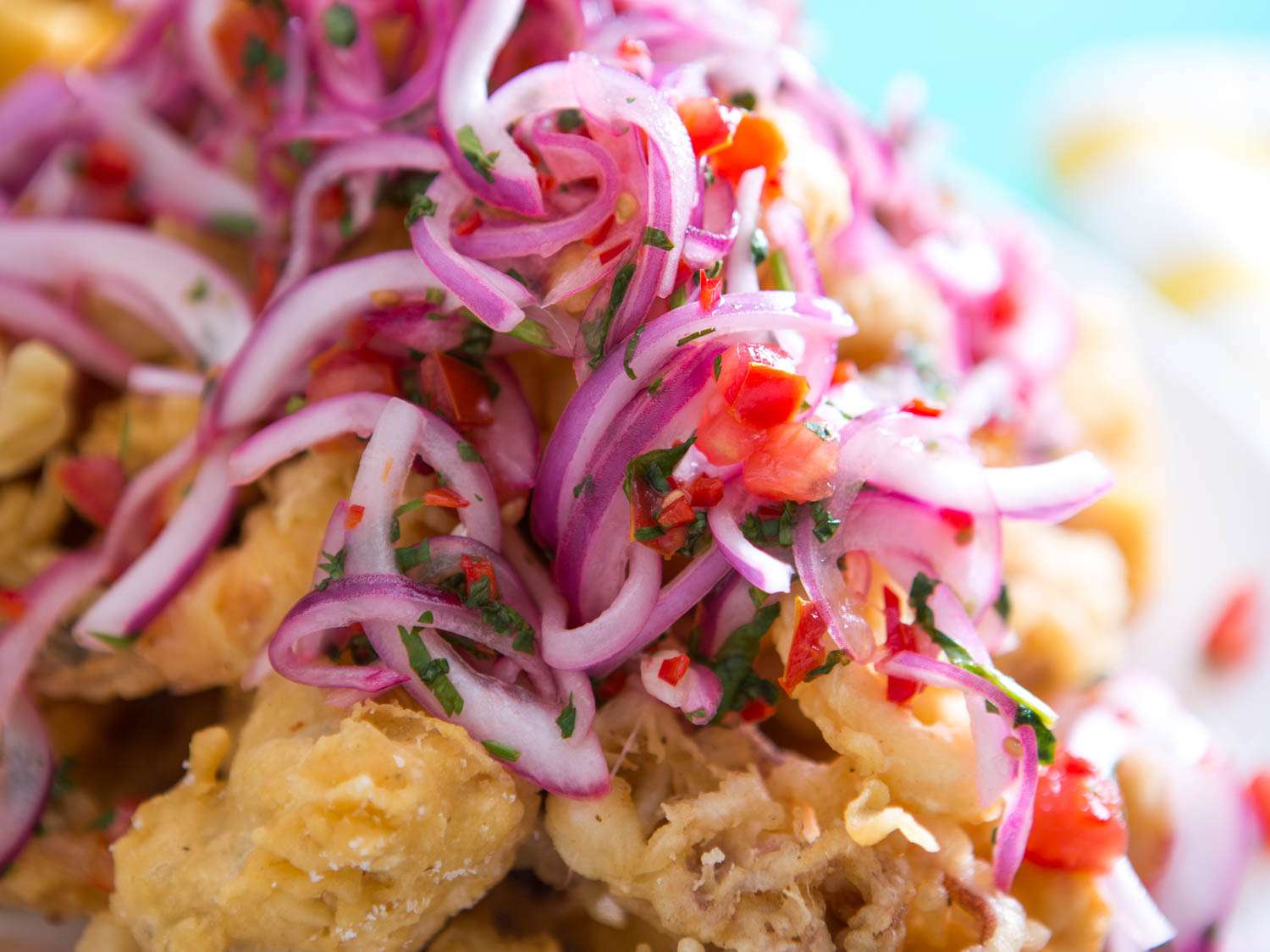 Close-up of sliced red onion, tomatoes, and cilantro piled on fried seafood