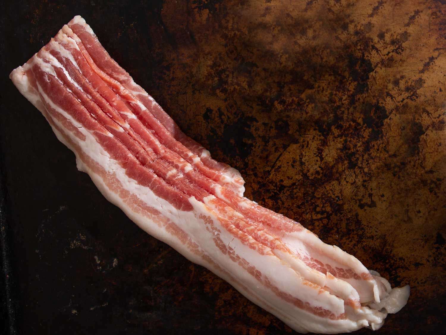 Raw bacon slices on a dark brown background.