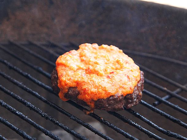 A burger on a grill with melted pimento cheese.
