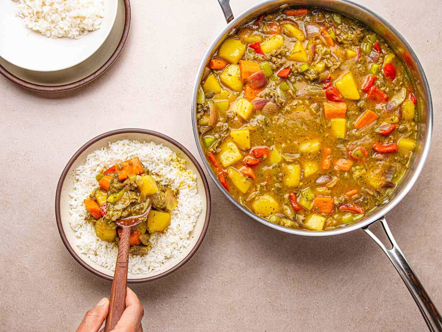 A bowl of white rice topped with Nigerian beef curry next to a pan of the curry being prepared