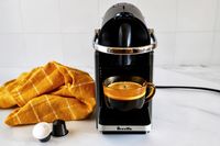 Breville espresso machine with a cup of coffee and coffee pods nearby