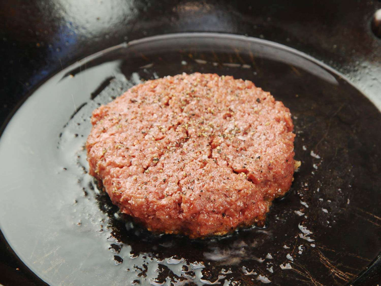 A seasoned burger patty made of Beyond Burger, frying in a cast iron skillet.