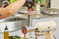 Person placing meat in food tray of KitchenAid KSMMGA Metal Food Grinder Attachment