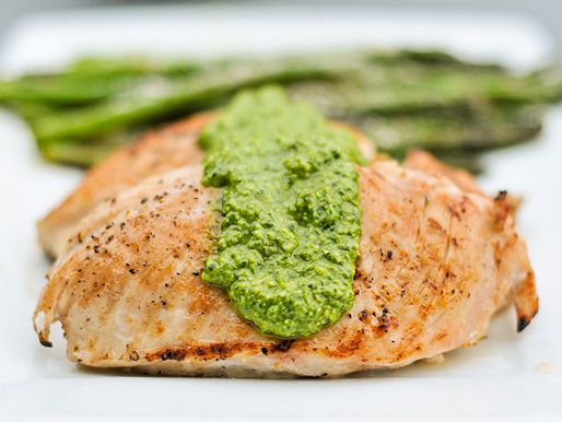 Profile view of grilled chicken breasts topped with a liberal dollop of arugula pesto.