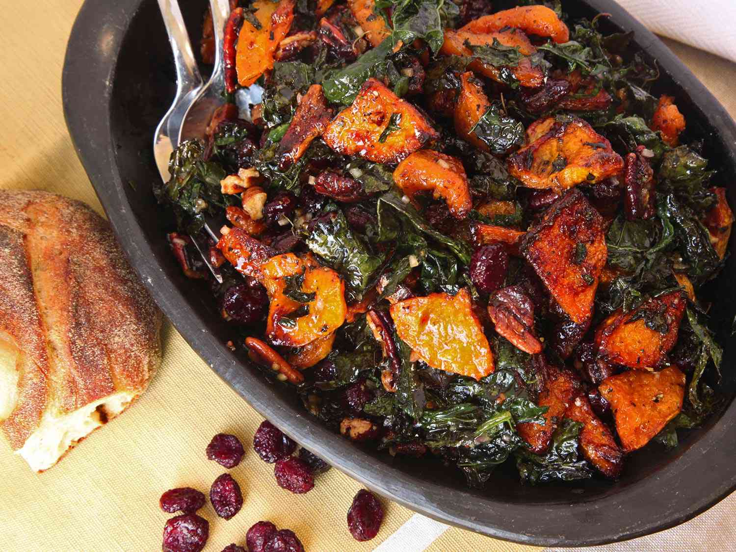 A finished roasted vegetable salad alongside bread and a handful of dried cranberries, ready to serve.