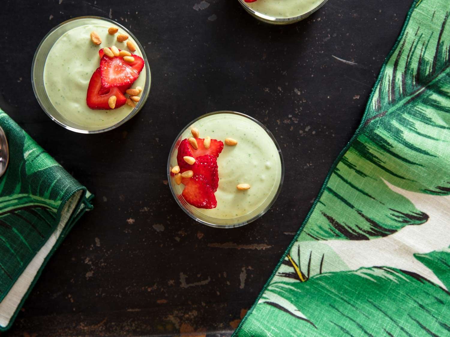 Overhead view of the finished, fruit-topped mousse, served in glasses on a black table next to green leaf-patterned napkins.