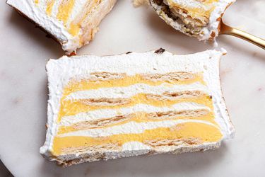 Overhead angle of 2 slices of Lemon Meringue Icebox cake on a marble plate. In the top right corner, there is a spoon with a bite of lemon meringue pie on it 