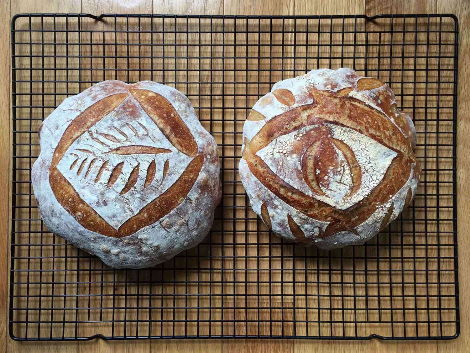 Two loaves of bread on a wire rack, one with an eye carved into it