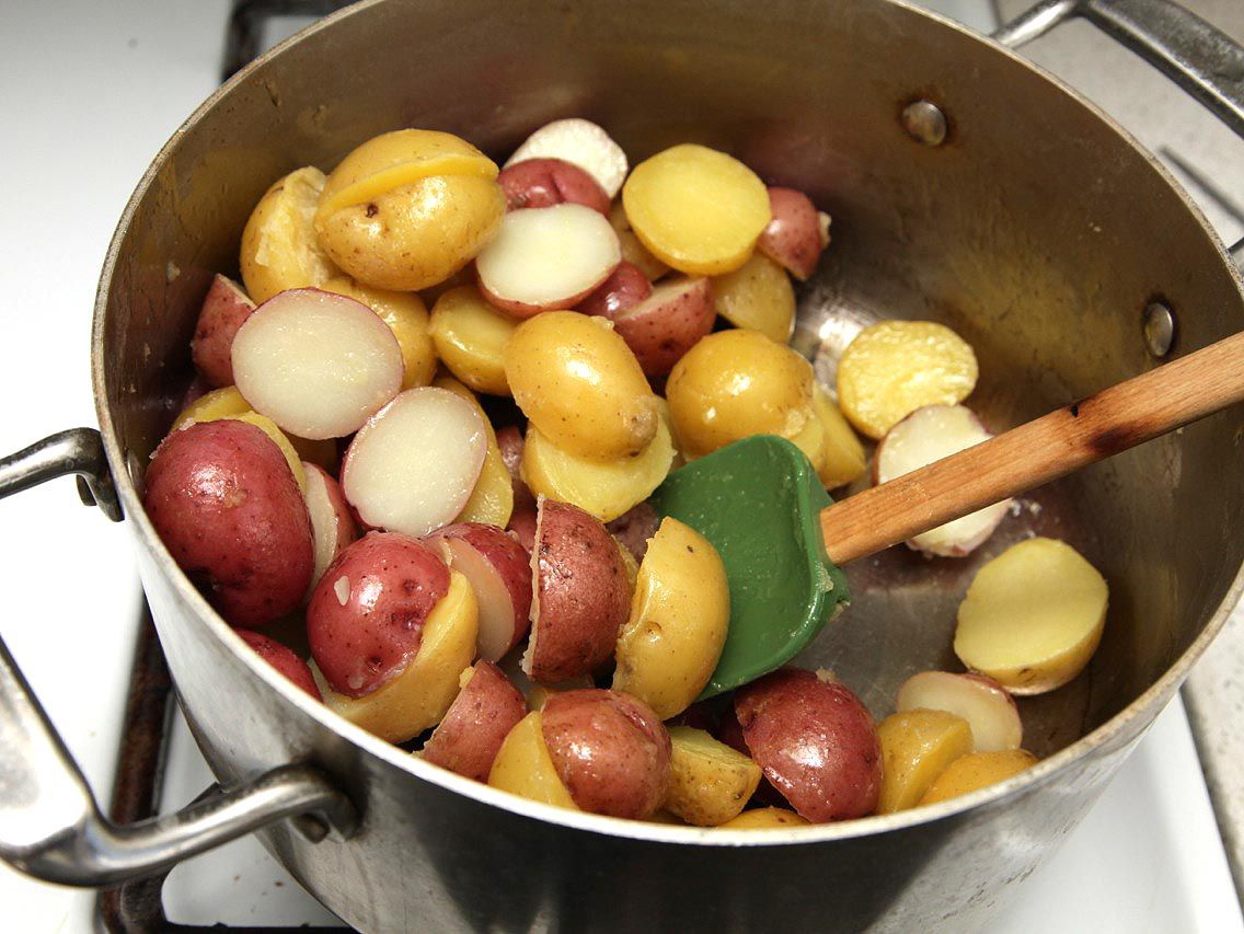 Spatula resting in pot with boiled and drained new potatoes.