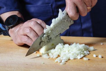 Two hands dicing an onion on a wooden cutting board.