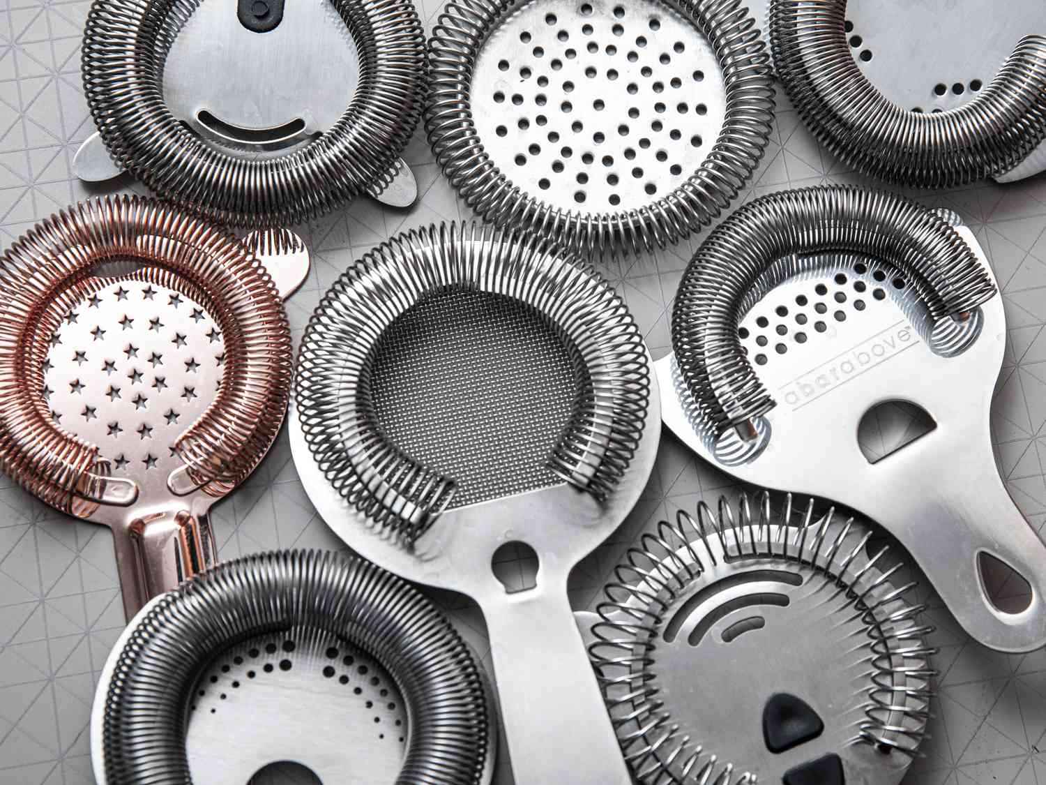 Numerous hawthorne strainers on a grey surface