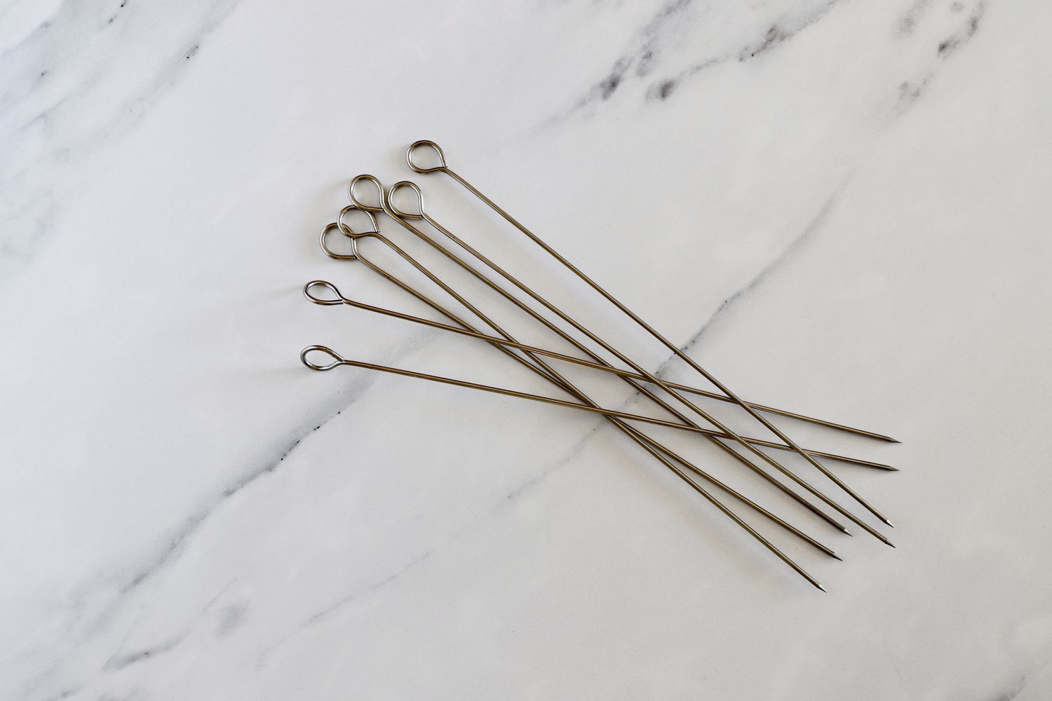 A handful of metal skewers on a marble surface