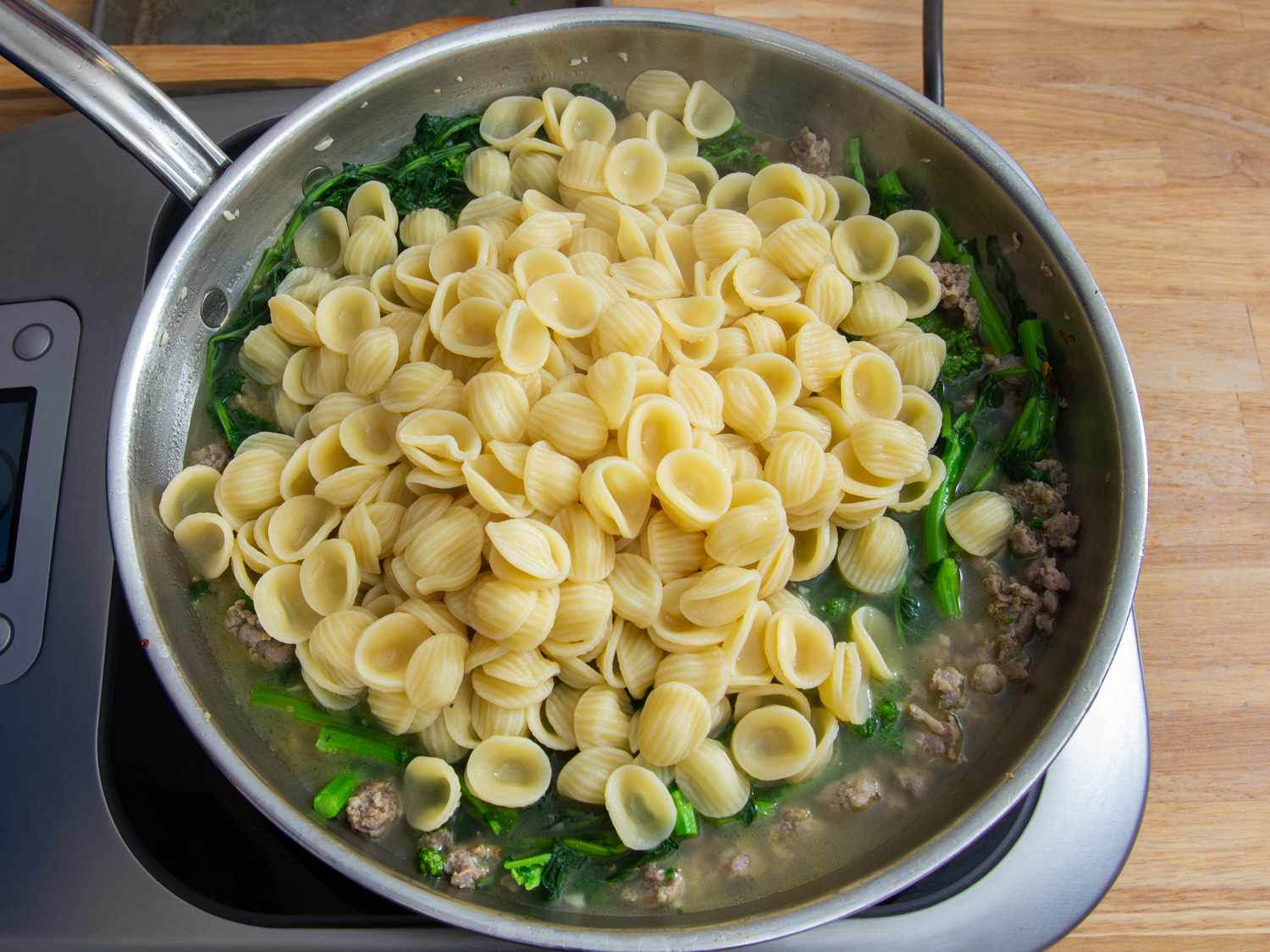 Al dente orecchiette on top of blanched broccoli rabe and cooked sausage in a skillet.