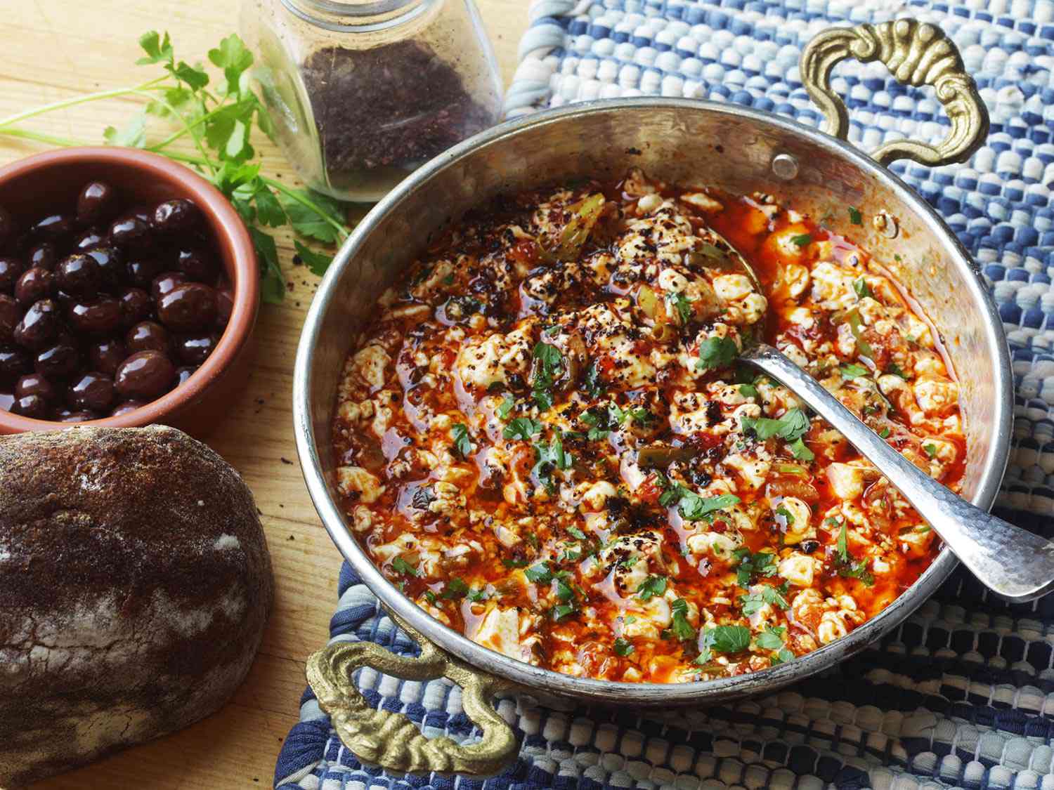 Turkish style vegan menemen in a Turkish style pan. There is a small dish of black olives next to it. .