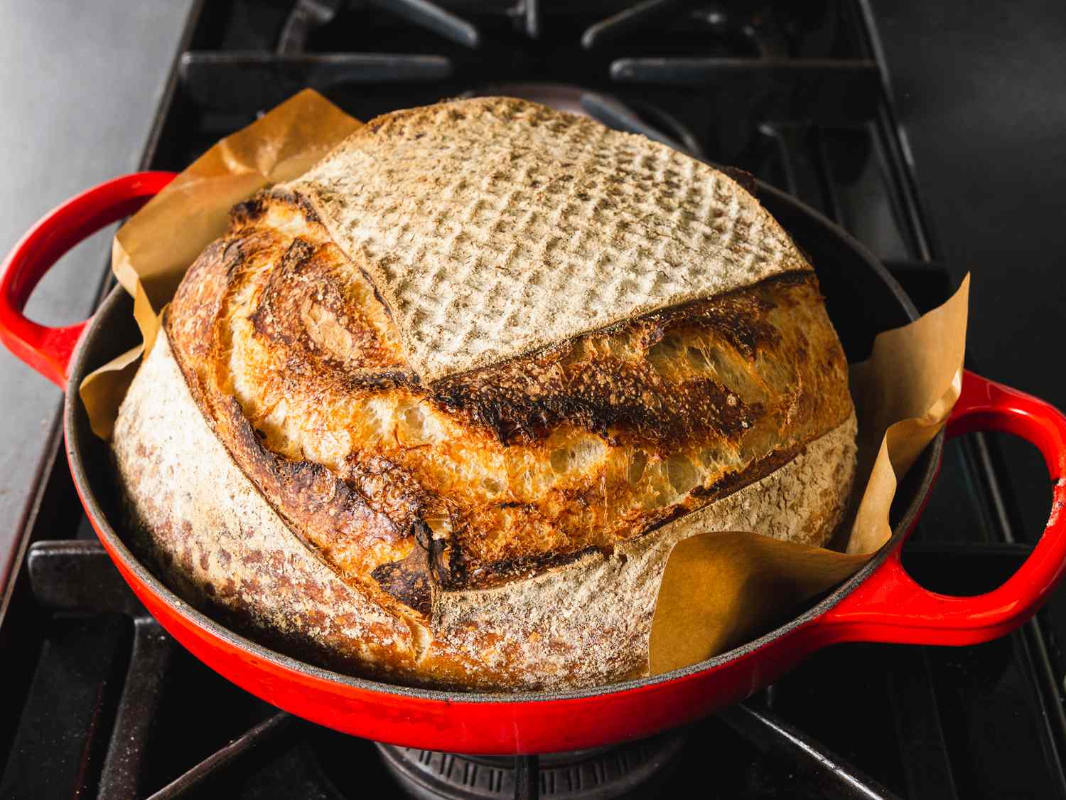 a loaf of bread made in a Le Creuset Bread Oven with a parchment paper sling beneath it