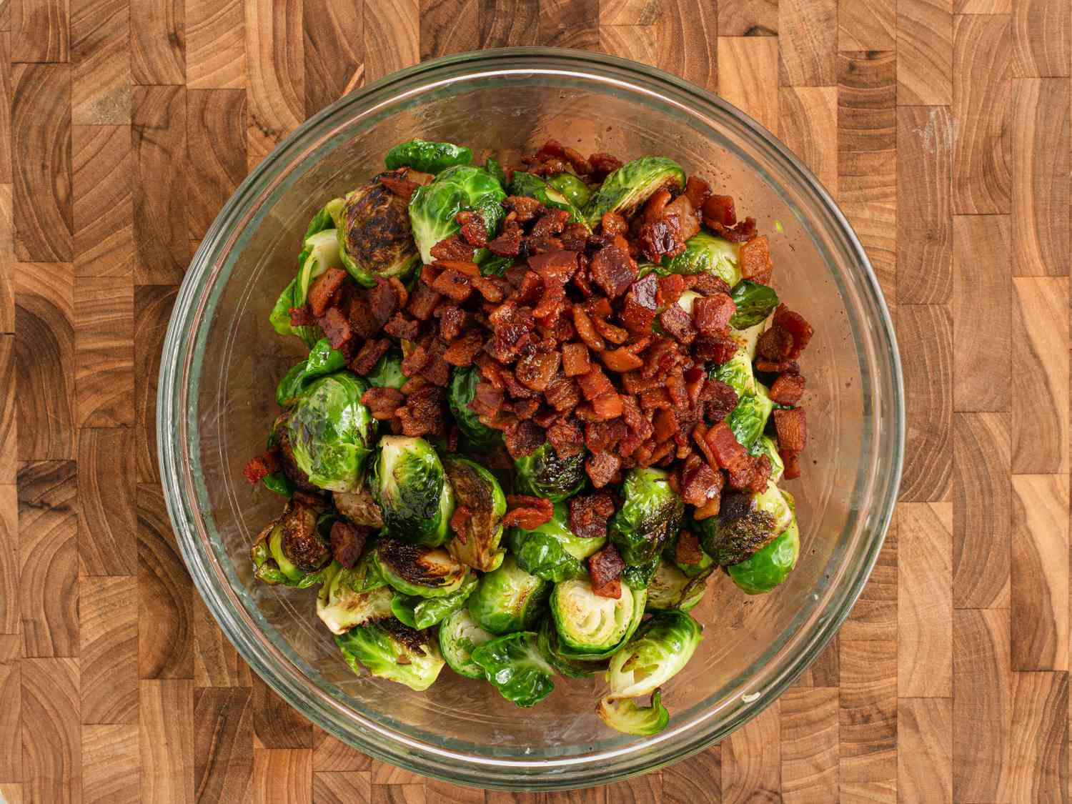 The browned Brussels sprouts and the cooked bacon inside of a glass bowl, before it was tossed together.
