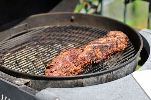 A lightly charred tenderloin cooking on a charcoal grill.