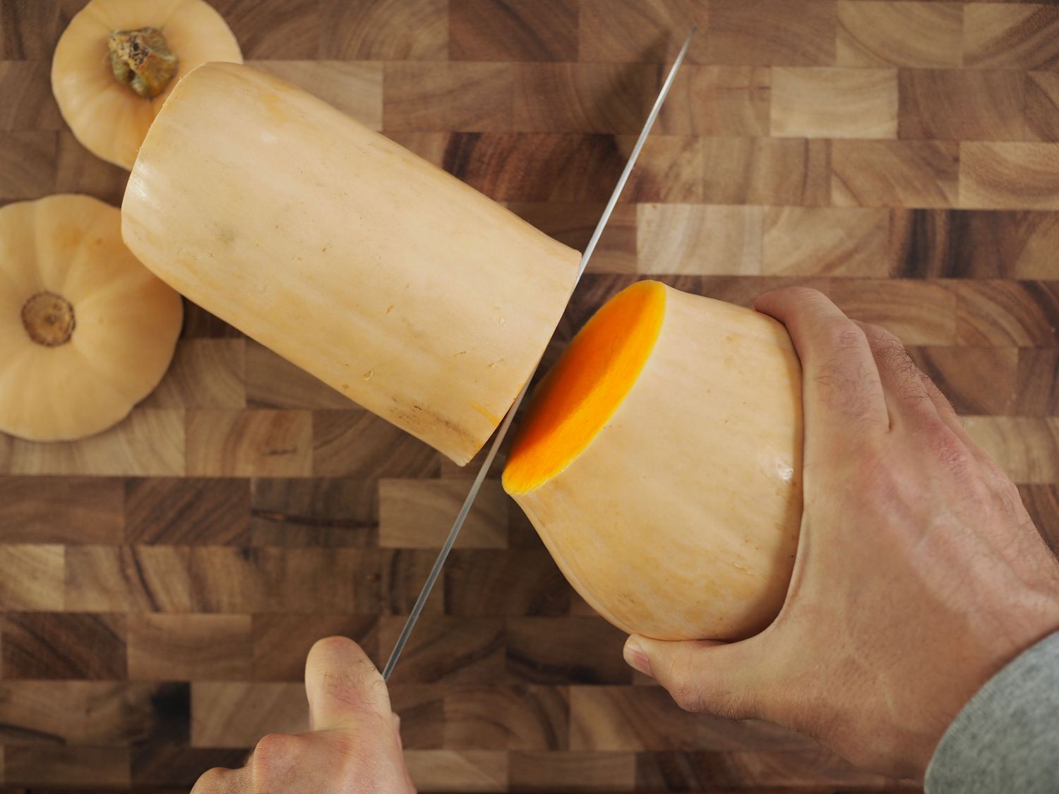 The neck of a butternut squash separating from the base thanks to a knife cut.