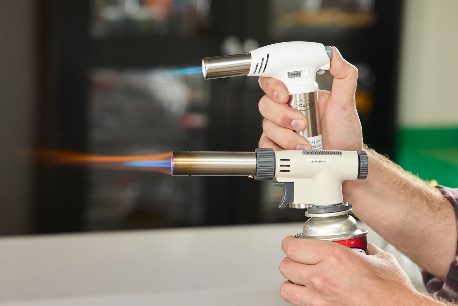 a person holding two different kitchen torches